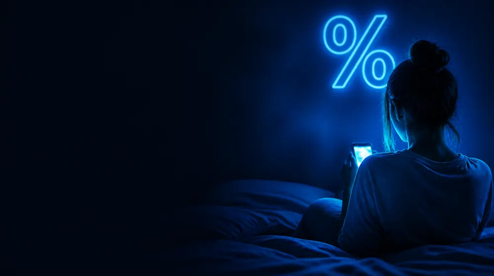 Cheap OnlyFans creators — woman on a bed lit by a smartphone glow, a neon percent sign glowing on the wall