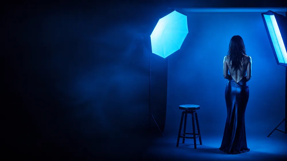 Model OnlyFans creators — woman posing under glowing softbox studio lights, a backdrop roll and posing stool set out