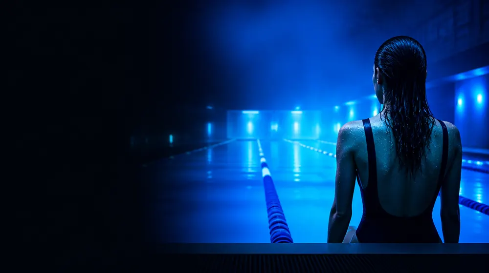 Swimmer OnlyFans creators — woman at the edge of a glowing pool at night, lane ropes shimmering down the lap pool